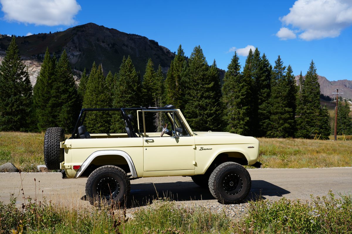 Driver-side front three-quarter view under a blue sky with pines and a mountain ridge behind